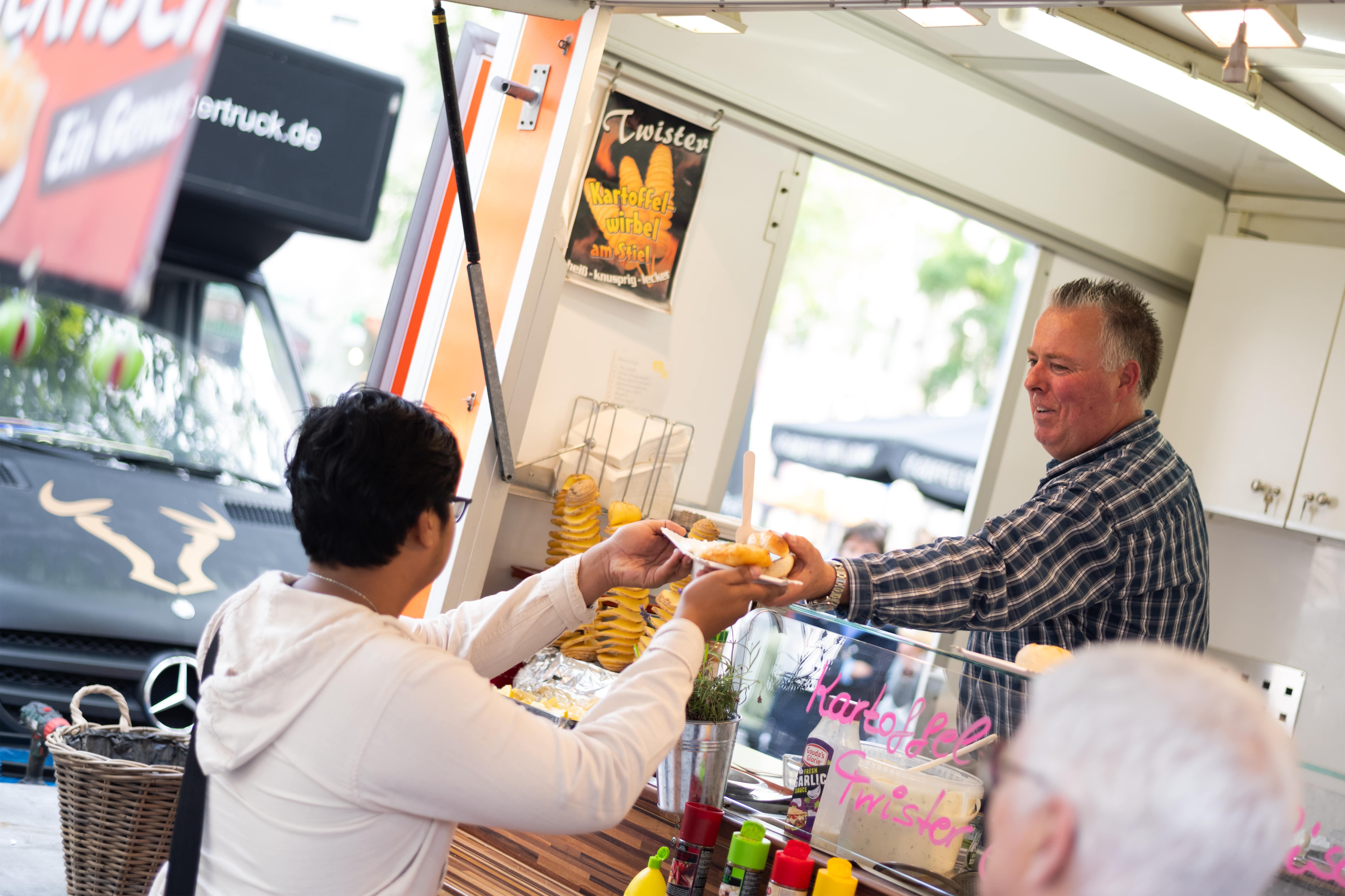 Kunde erhält frische Kartoffel-Twister an einem Foodtruck auf dem Feierabendmarkt am Chlodwigplatz in Köln.