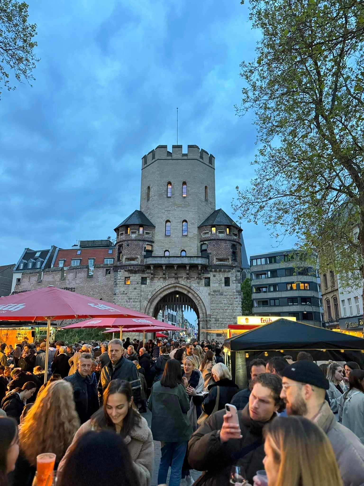 
Menschenmengen genießen den Feierabendmarkt am Chlodwigplatz in Köln bei Abendstimmung vor dem Severinstor
