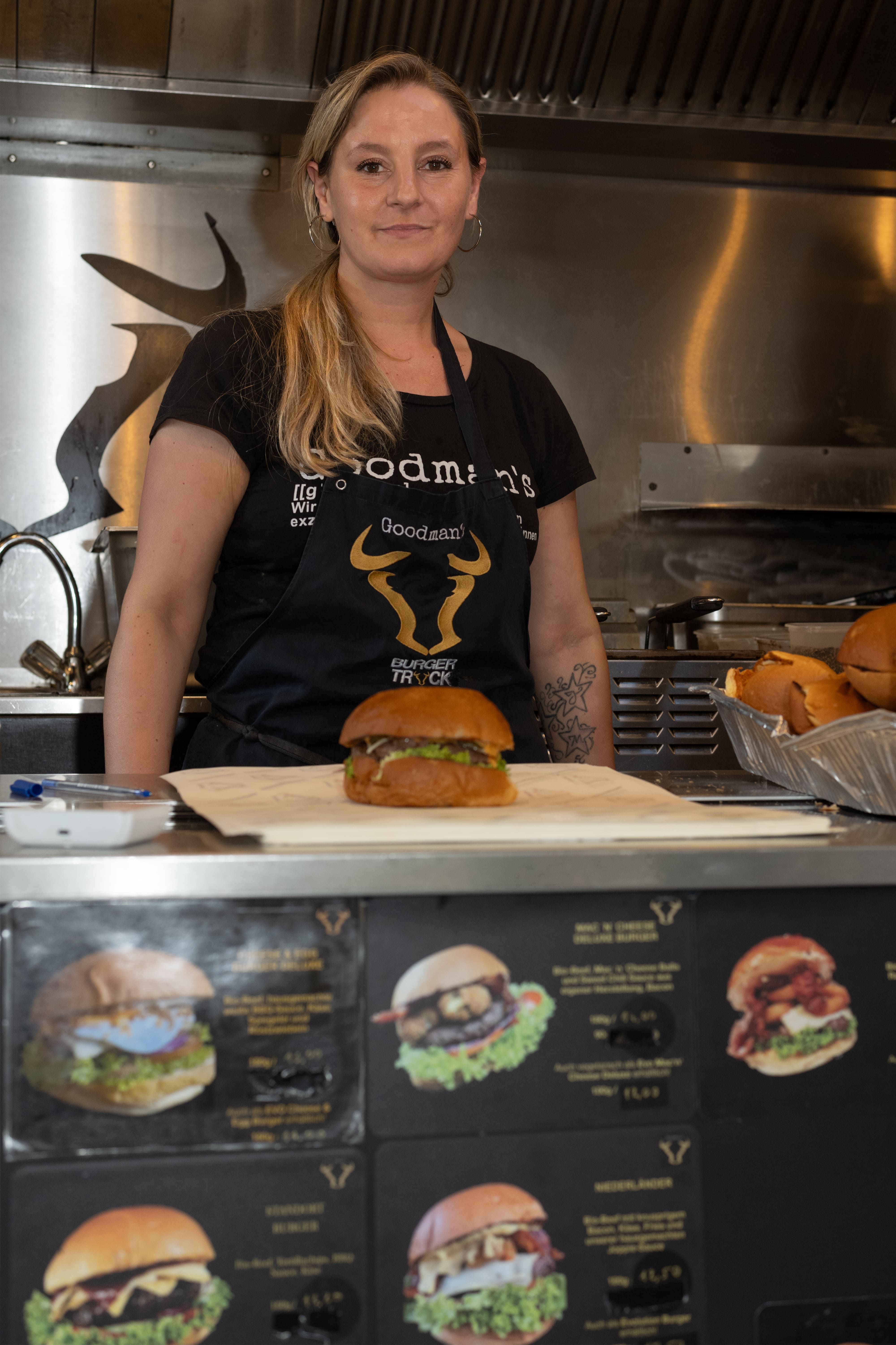 
Foodtruck-Mitarbeiterin serviert einen frisch zubereiteten Burger auf dem Feierabendmarkt am Chlodwigplatz in Köln
