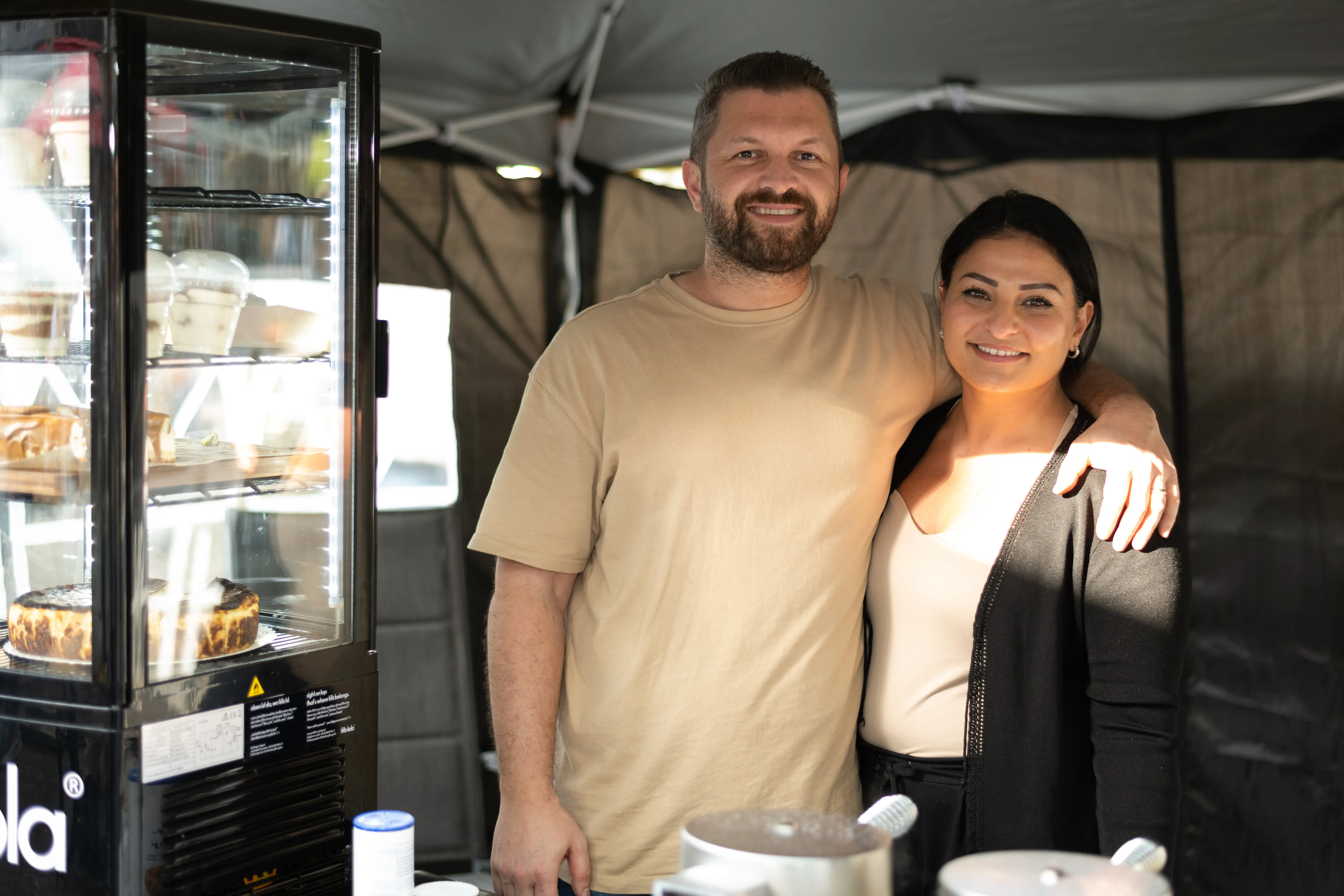 
Ein Streetfood-Stand mit einem lächelnden Paar, das auf dem Feierabendmarkt am Chlodwigplatz in Köln Spezialitäten anbietet.

