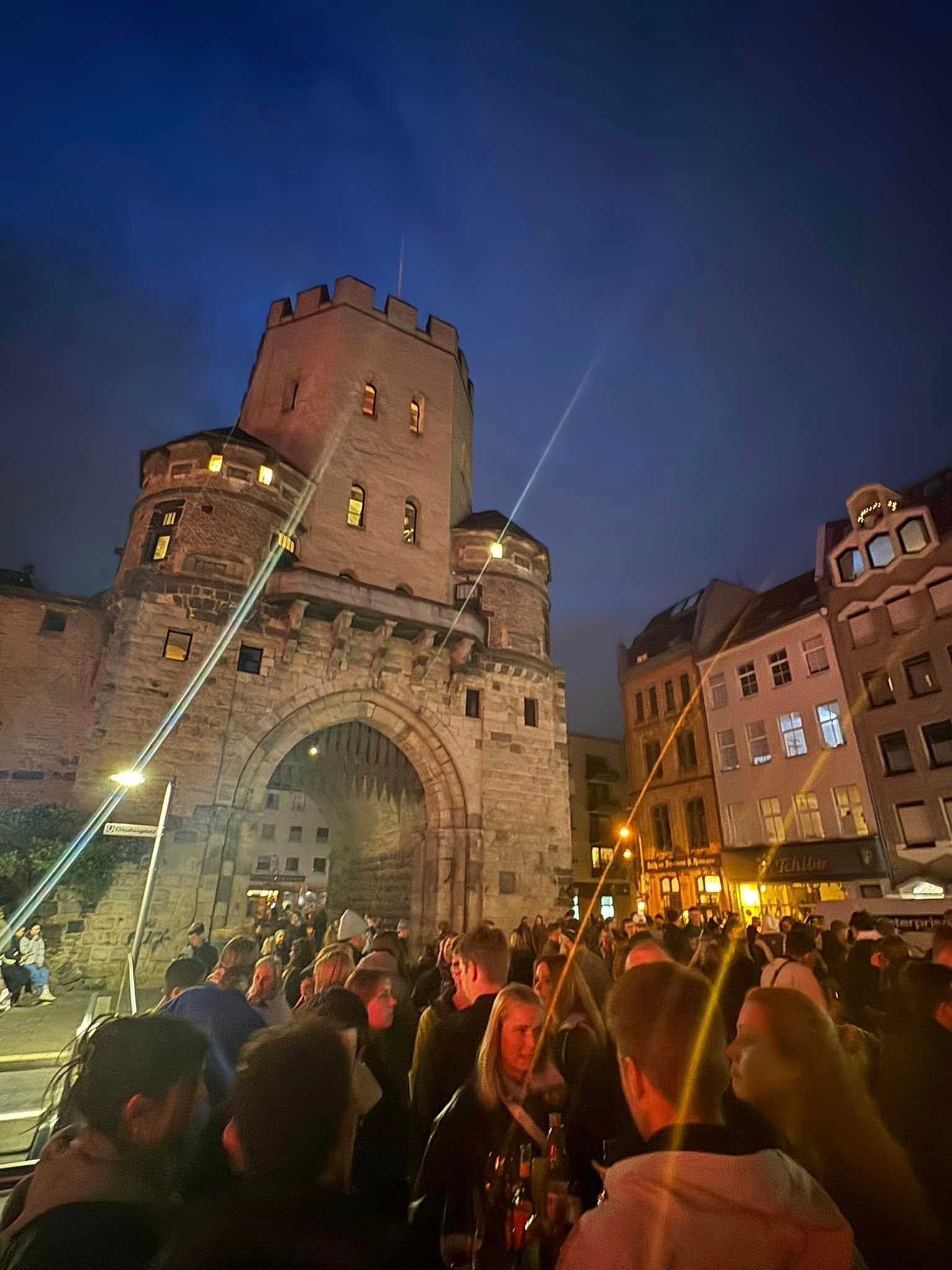 
Menschen genießen den Feierabendmarkt am Chlodwigplatz in Köln bei Nacht vor dem Severinstor
