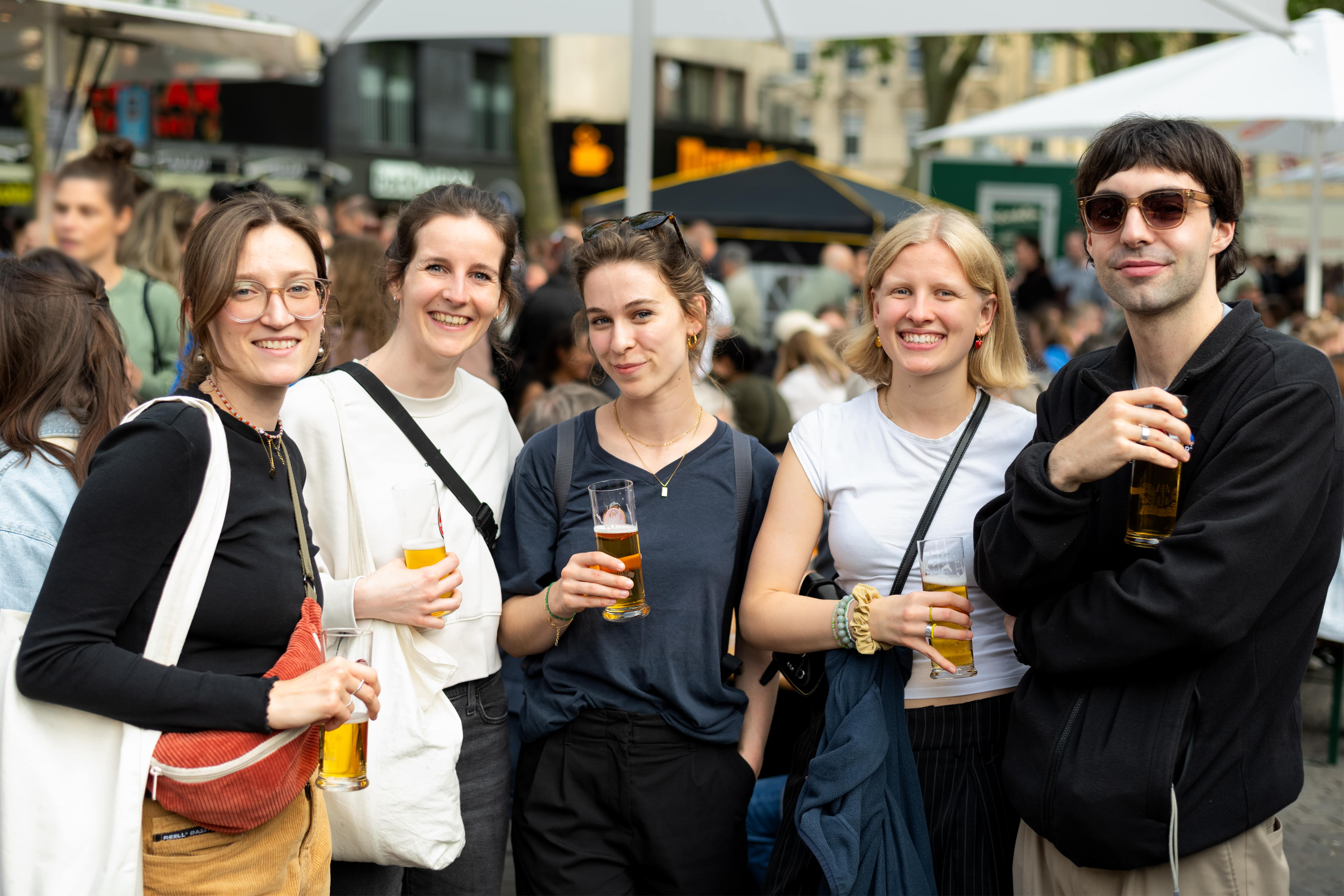 Menschen stoßen auf dem Feierabendmarkt in Köln mit Aperol Spritz und Kölsch an. Die Atmosphäre ist lebendig und entspannt.