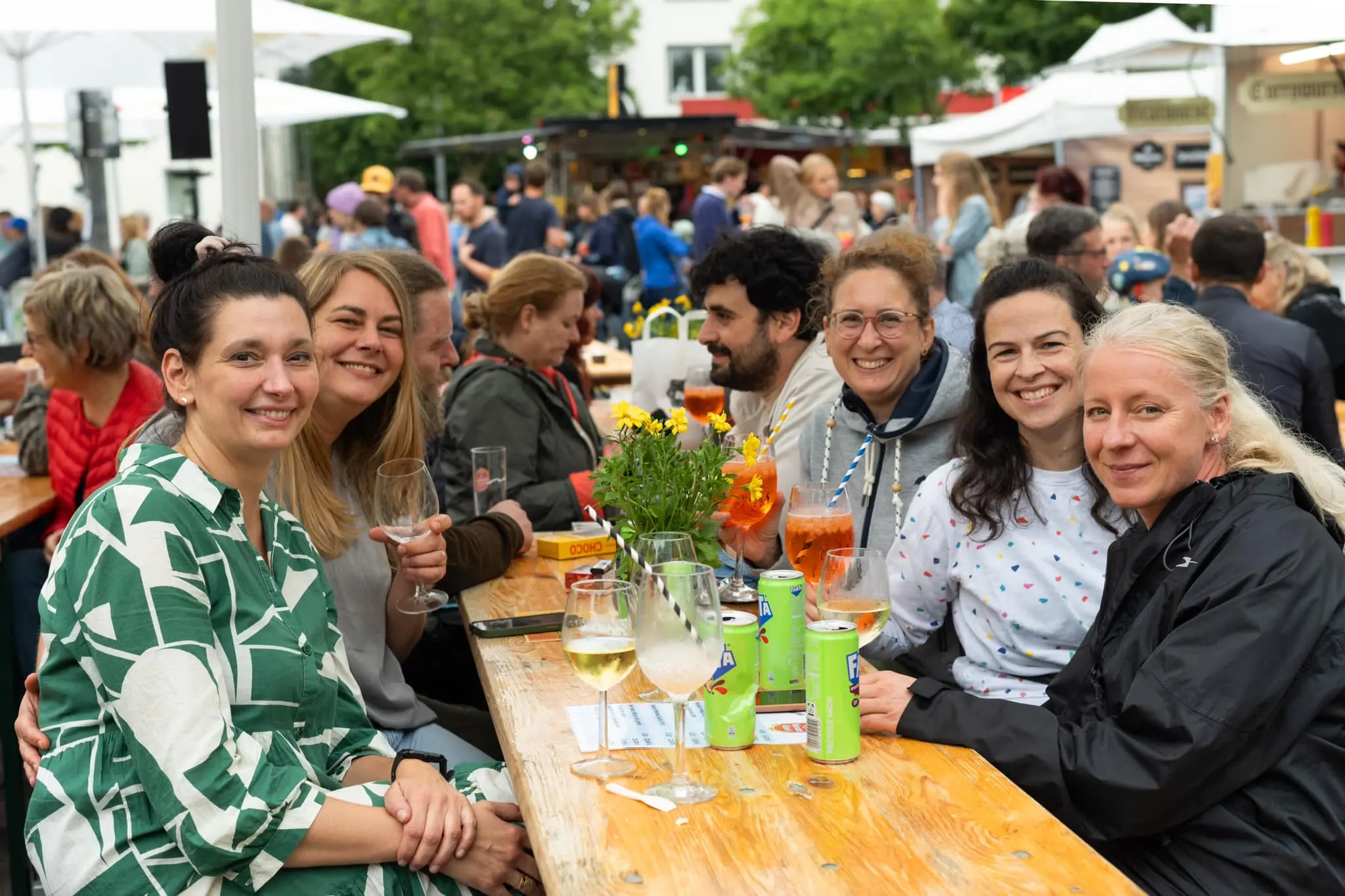 Eine fröhliche Gruppe von Frauen sitzt an einem Holztisch und genießt gemeinsam Drinks