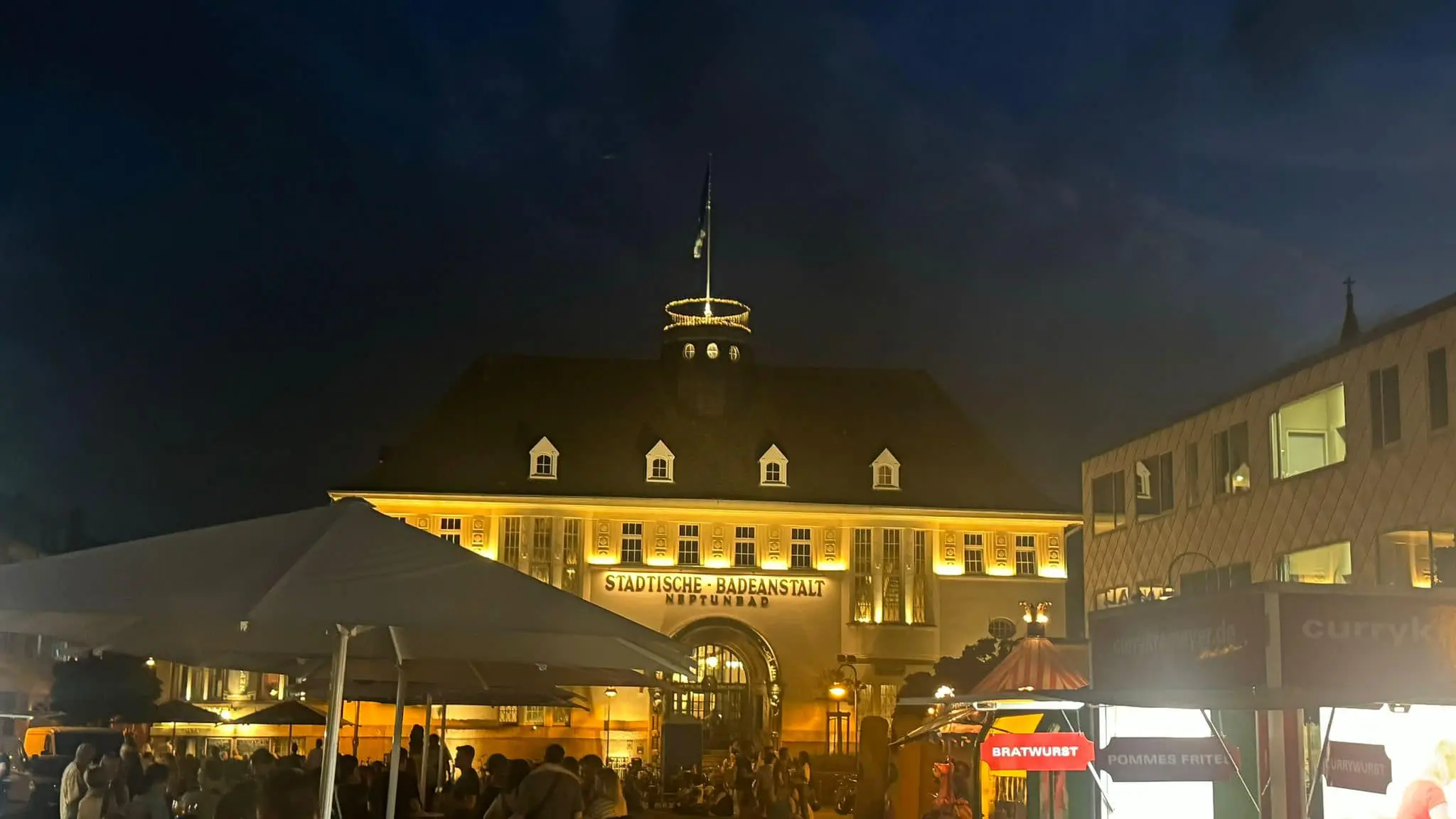 Das Neptunbad in Köln strahlt in stimmungsvoller Beleuchtung während des Feierabendmarkts bei Nacht