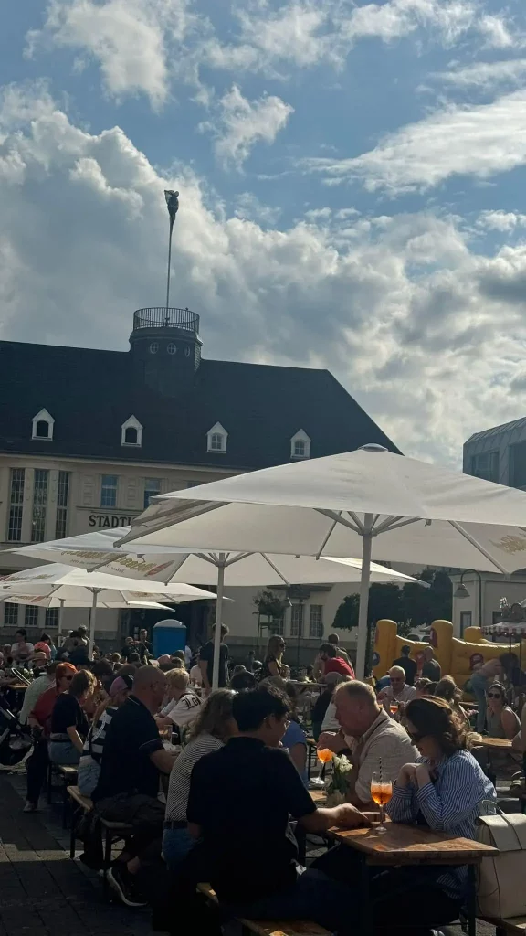 Menschen sitzen bei sommerlichem Wetter mit Aperol Spritz und Bier auf dem Feierabendmarkt am Neptunplatz in Köln