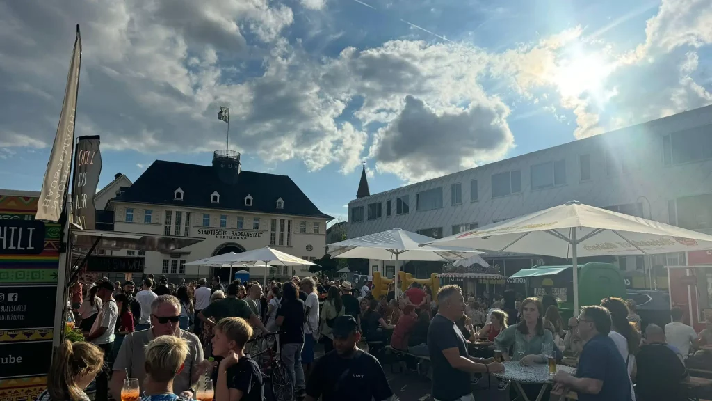 Menschen genießen den Feierabendmarkt am Neptunplatz in Köln bei Sonnenschein mit Foodtrucks und Biergarten-Atmosphäre.